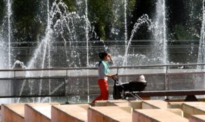 Una mujer pasea un carrito al lado de una fuente para protegerse del calor